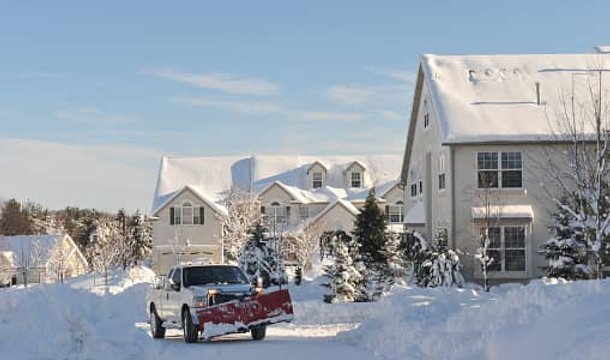 A truck with a snow plow attachment clearing a road on a snowy day.